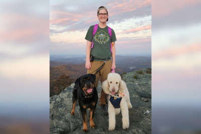 Christa White (at center) standing on a rock with her dogs, a rottweiler (at left) and a poodle (at right)