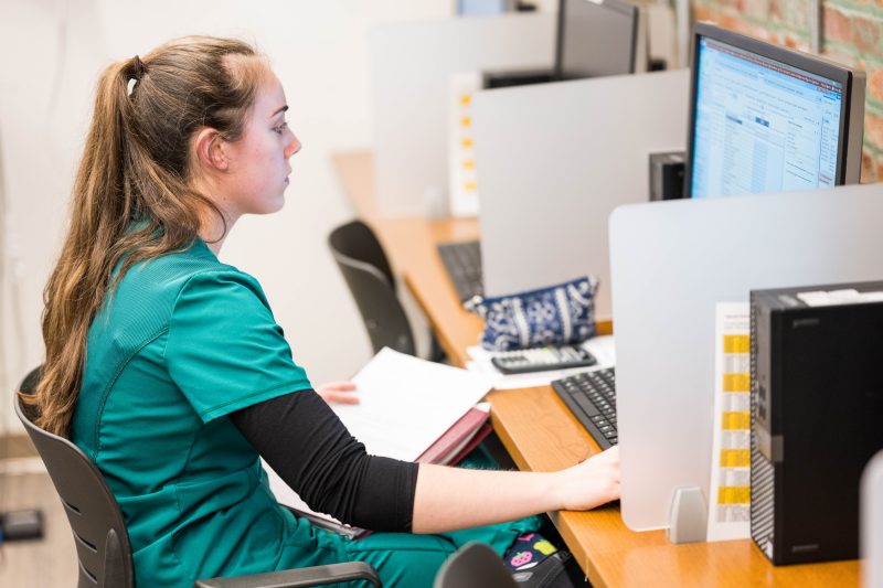 A Virginia Tech MSND student sits at a computer and runs calculations prior to visiting with a patient.