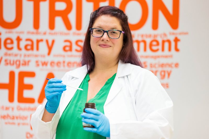 A Virginia Tech HNFE faculty member stands holding a spoonful of an artificial sweetener in a lab.